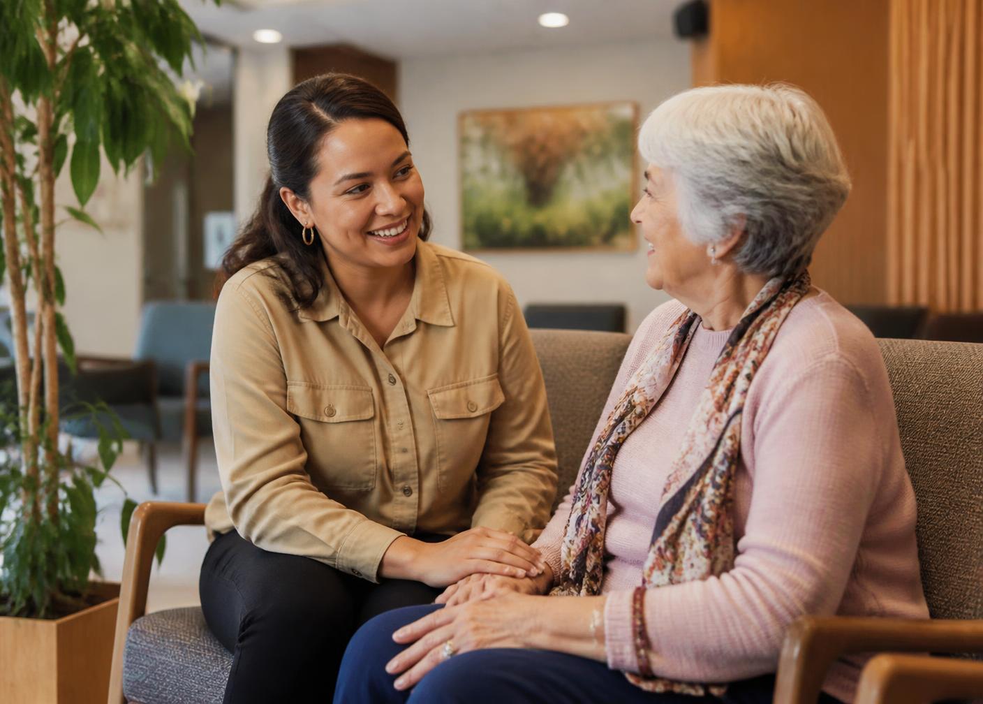 A companion sitting and talking with a senior woman in a comfortable waiting area
